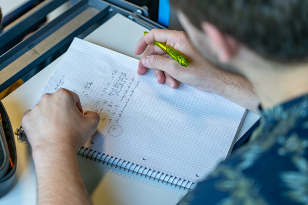 Männlicher Student schreibt in einer Physik-Vorlesung etwas auf einem Block mit.