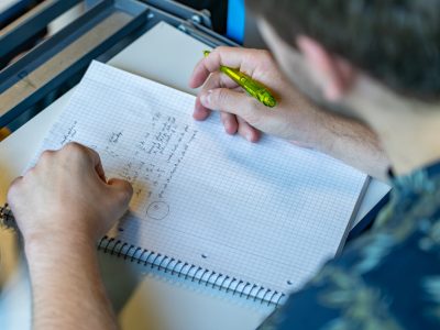 Männlicher Student schreibt in einer Physik-Vorlesung etwas auf einem Block mit.